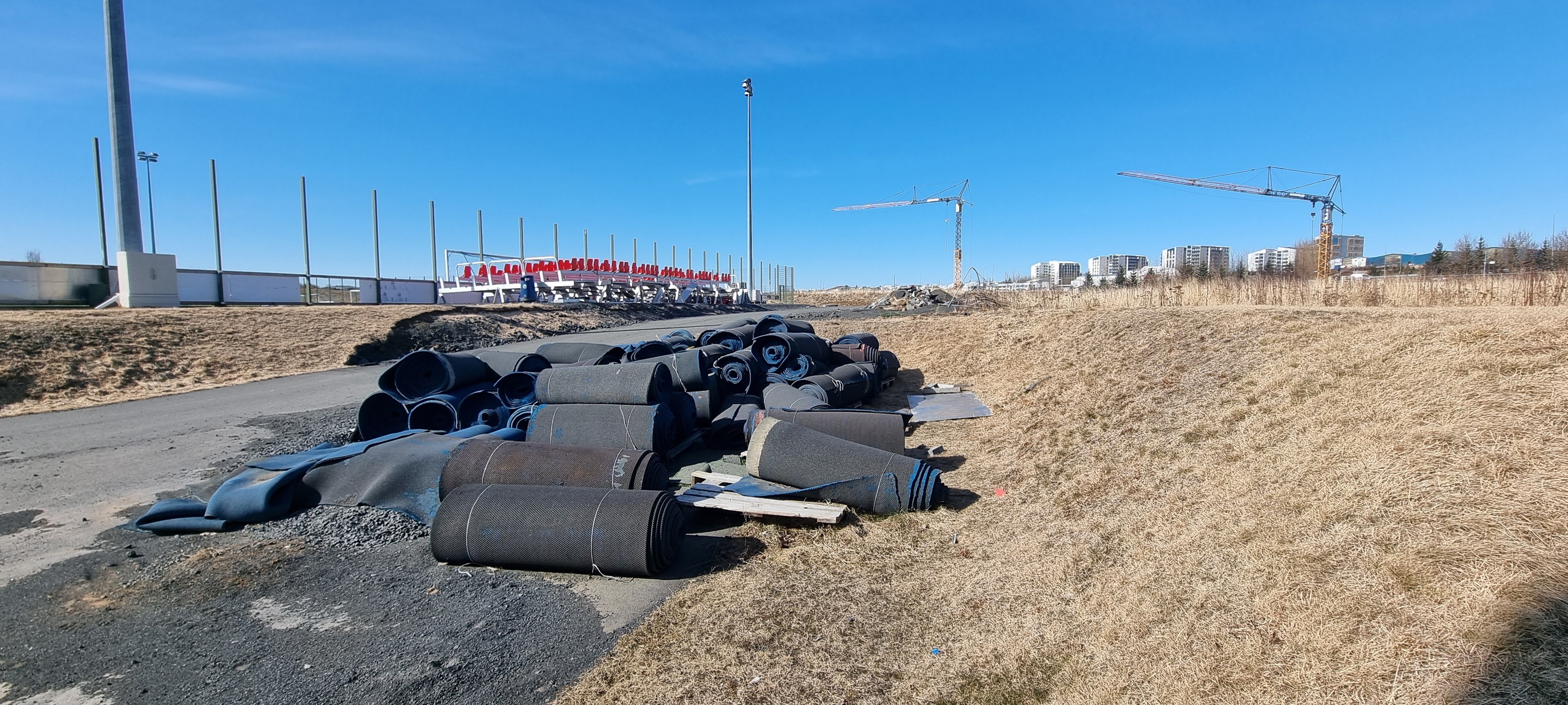 Malbiksrúllur dumpaðar á göngustíg við ÍR-svæðið, með krana í bakgrunni.
